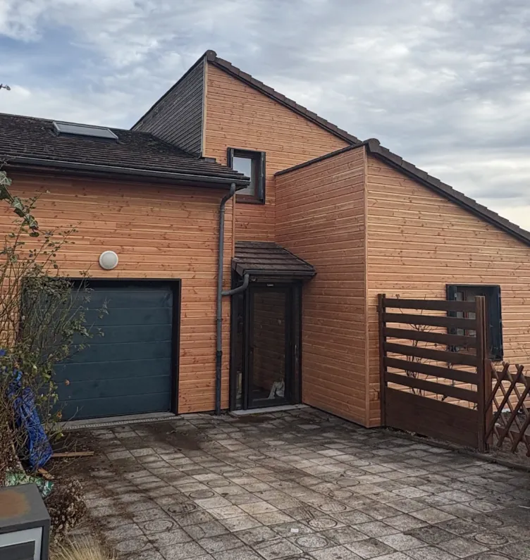 Maison à bardage bois vertical avec porte de garage grise