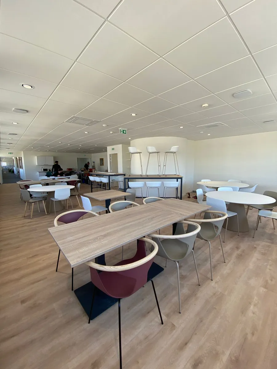 Salle de réfectoire avec tables et chaises sur parquet clair